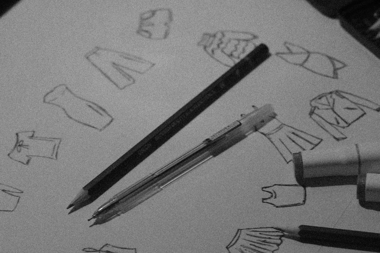 Hand-drawn vector sketches of clothing shapes on paper beside a pencil and pen, with a tablet and laptop nearby